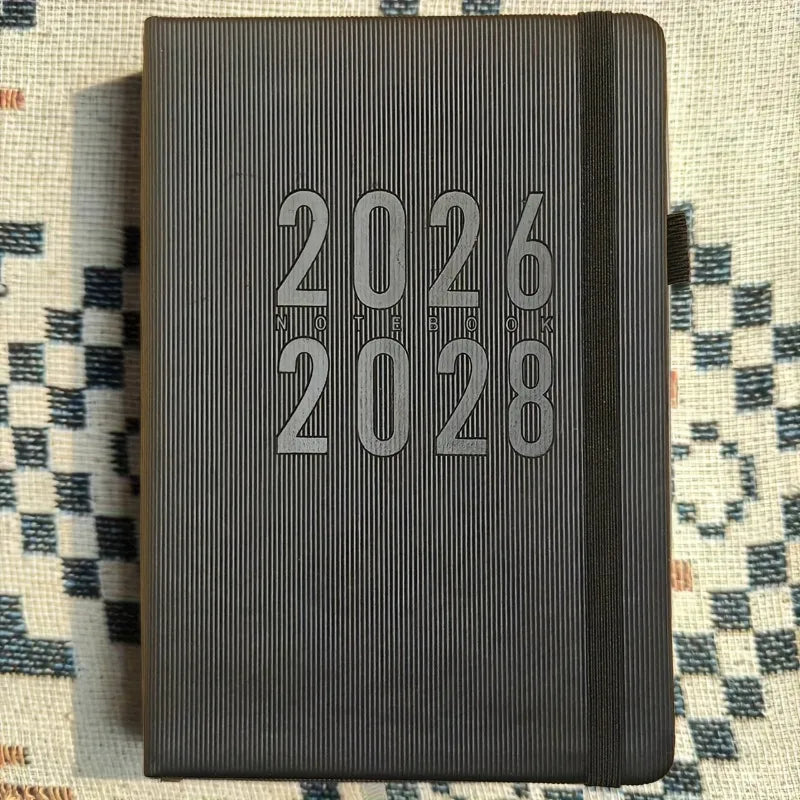 Black planner with '2026' and '2028' text on a patterned fabric background
