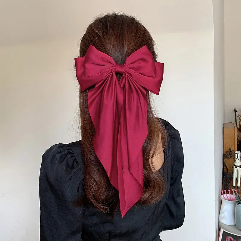 Person wearing a large red bow in their hair against a plain background
