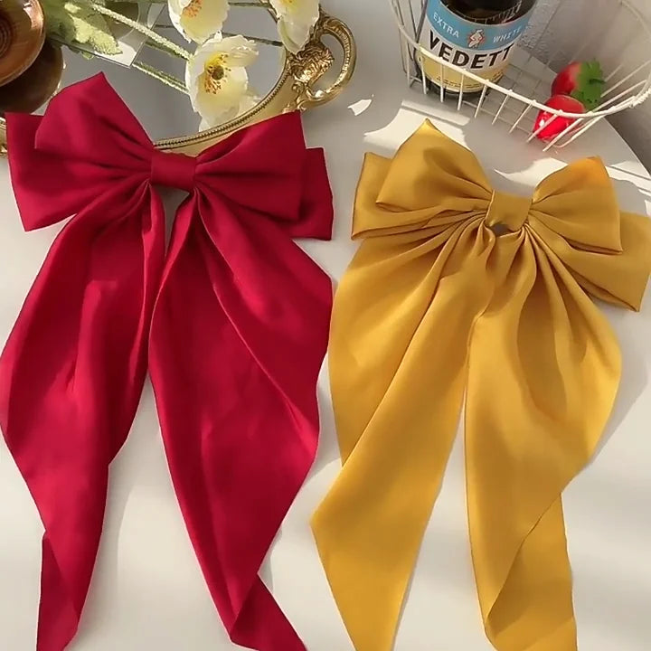 Two large fabric bows, one red and one yellow, on a white surface with a blurred background.