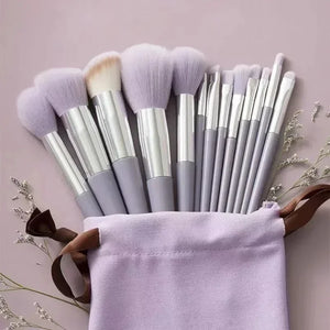 Set of makeup brushes with purple bristles in a drawstring bag on a light pink background