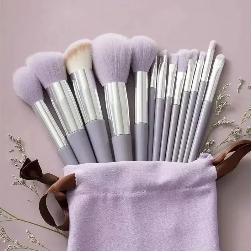 Set of makeup brushes with purple bristles in a drawstring bag on a light pink background