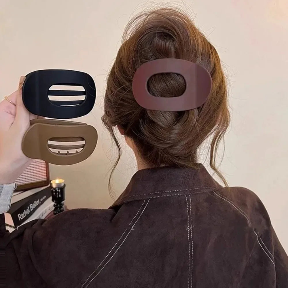 Person with a hair bun wearing a hair clip, holding three different hair clips in front of them.