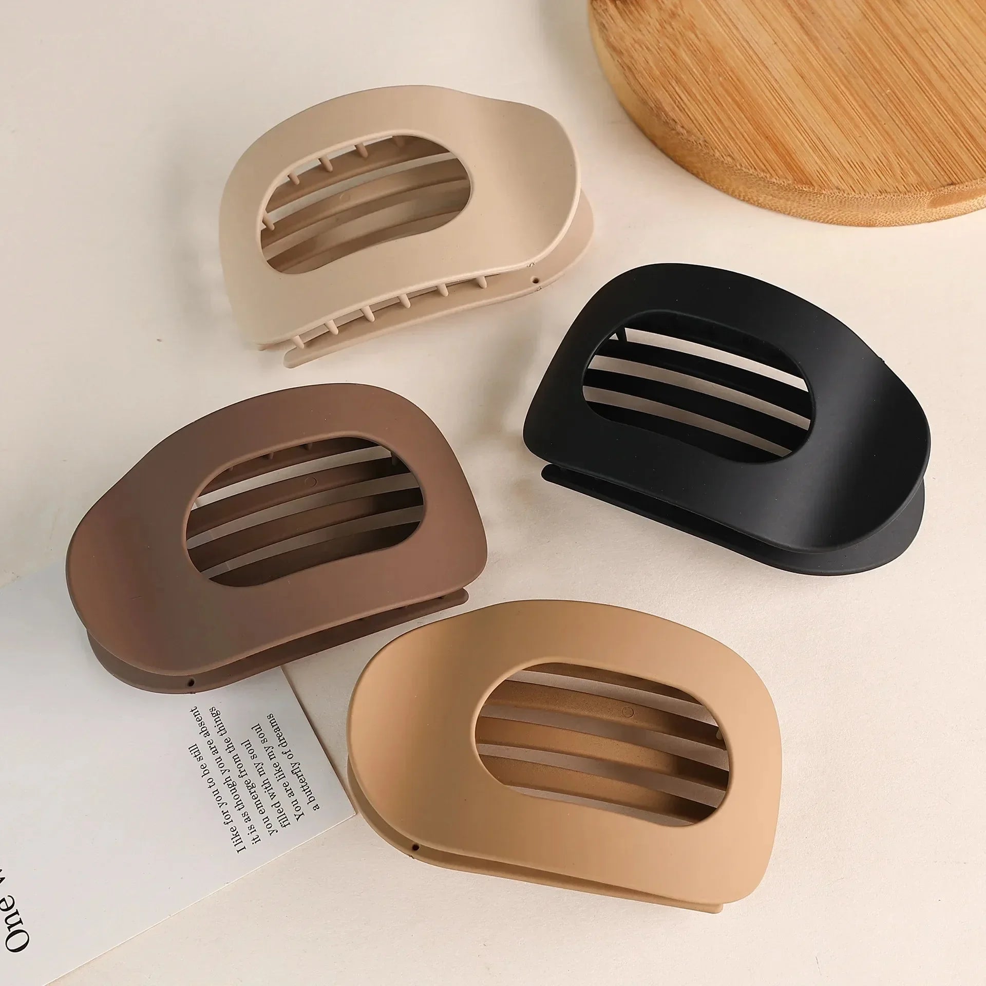 Four soap dishes in beige, brown, and black on a light surface with a wooden board in the background.