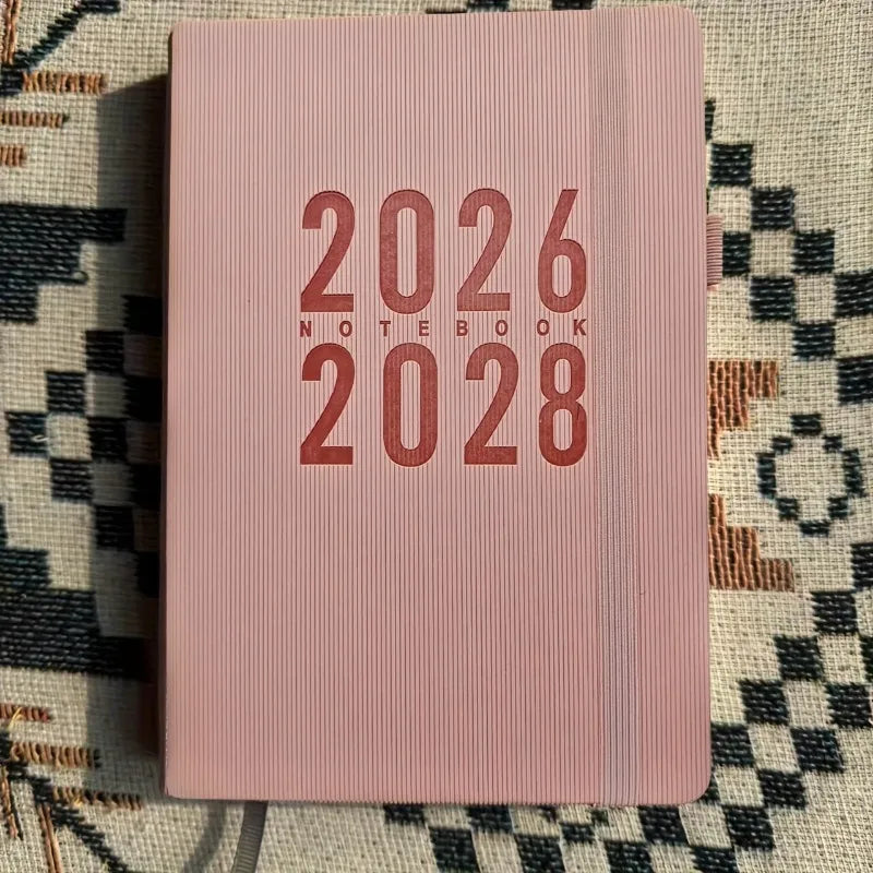 Pink notebook with '2026 Notebook 2028' text on a patterned surface