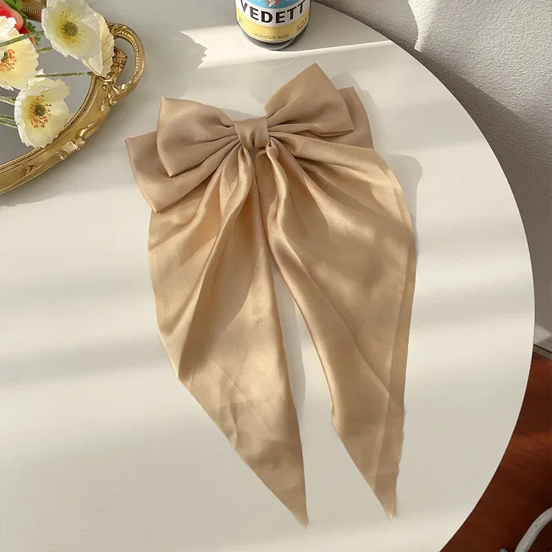 Beige bow scarf on a white surface with a mirror and flowers in the background
