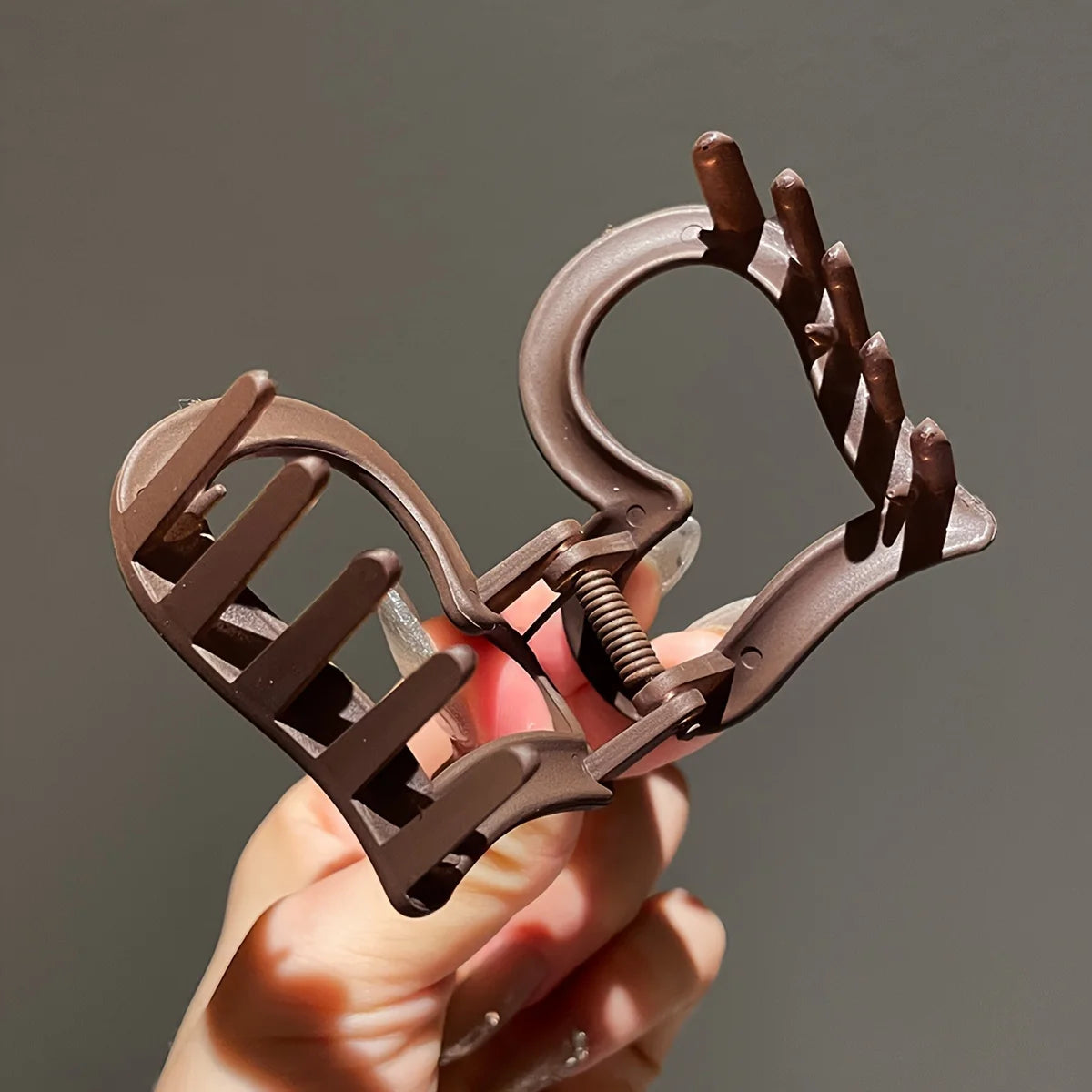 Brown metal bottle opener held by a hand against a gray background