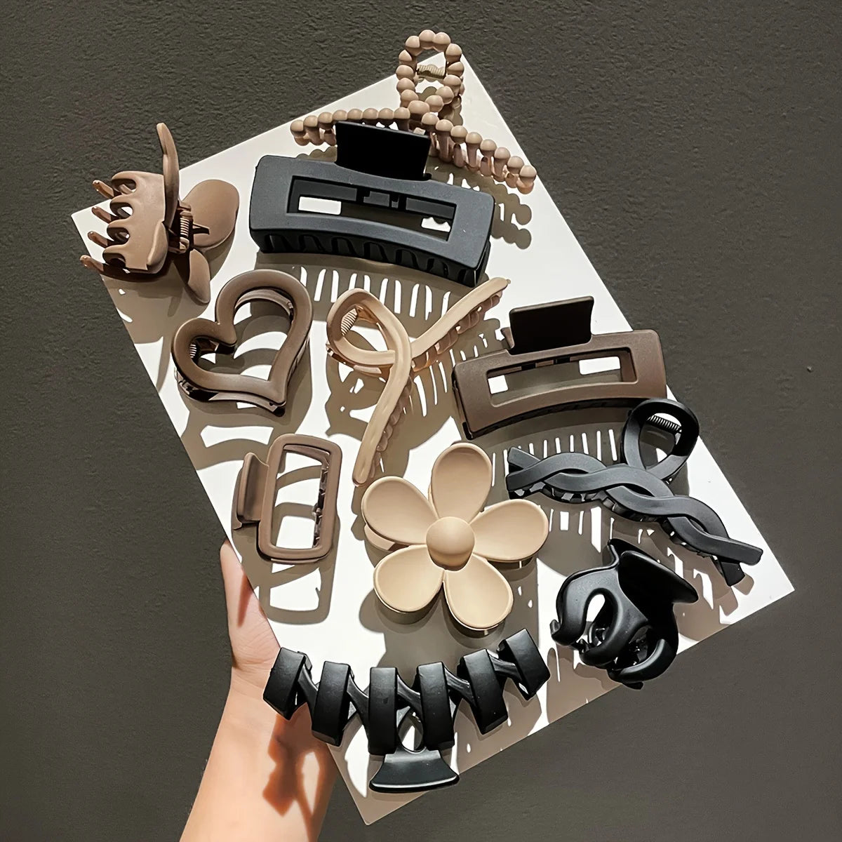 Collection of various hair clips on a white square with a hand holding it against a dark background